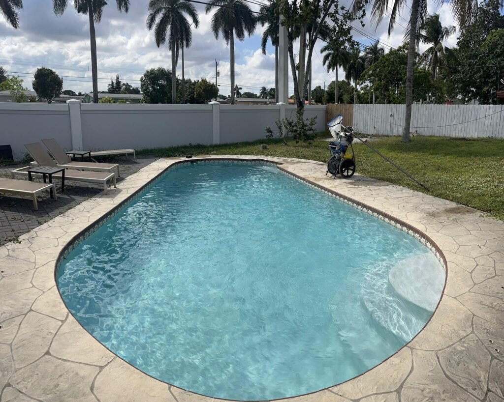 Piscina de forma libre rodeada de palmeras, con el agua limpia y la tumbona al borde